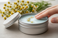 large wide silver tin with light blue balm ,chamomille in the background and soft skin