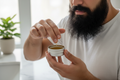 muslin 20 year old appling beard oil to his long black beard from a plain 30 ml tin contsainer